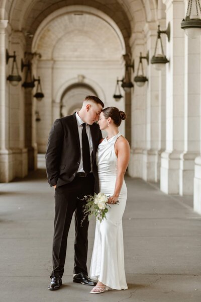 A wedding couple stand under the archways of Union Station in an almost kiss during their Washington DC elopement.
