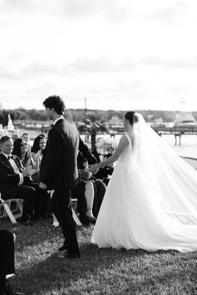 A bride and groom share a romantic dip kiss at their outdoor wedding, framed by white chairs and a backdrop of illuminated trees.