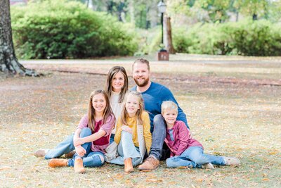 a happy family sits in the grass in jeans smiling and snuggling