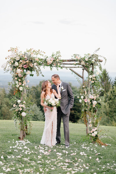 Bride & groom framed by a lush pastel ceremony arch
