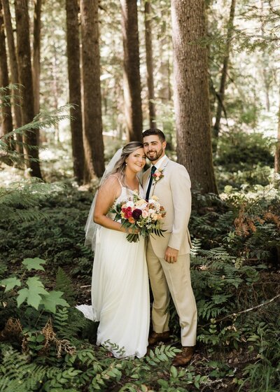 A bride and groom in the forest with the bride holding her bouquet, by Eugene Florist Flowers and Thyme.