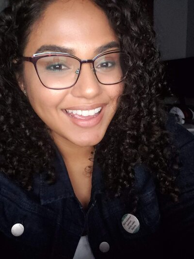 Afro-Latinx woman with long curly hair and glasses