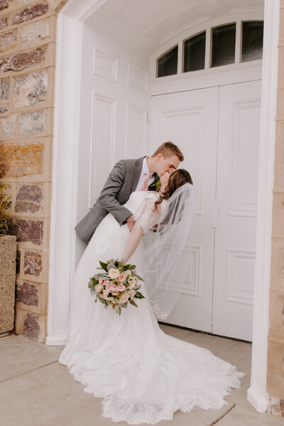 bride and groom kissing outside LDS temple bride holding light pink roes bouquet