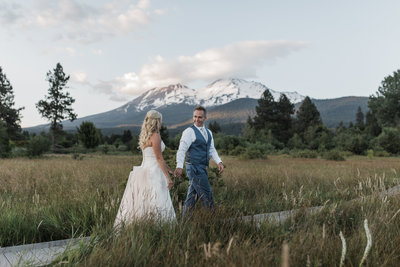 bride and groom walking in field with snow covered mountains in background