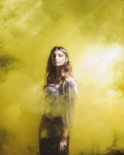 Jeune femme sure d'elle, debout, regardant l'objectif, enveloppée de fumée jaune néon.