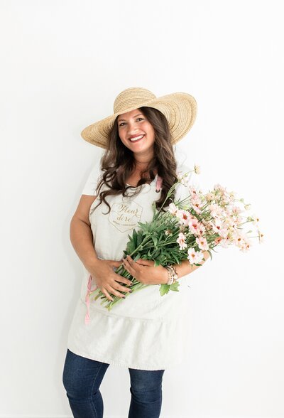 Fleur Di Ri owner holding bouquet and wearing apron and sun hat 