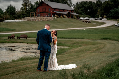 Couple reads private vows to eachother by a pond in front of a red barn as they laugh together. 