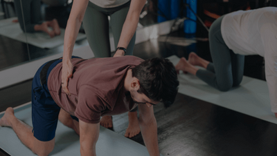 pilates teacher giving hands on assistance to a client in a mat pilates class 