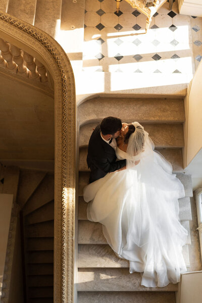 Overhead image of bride and groom kissing on stairs of a French chateau