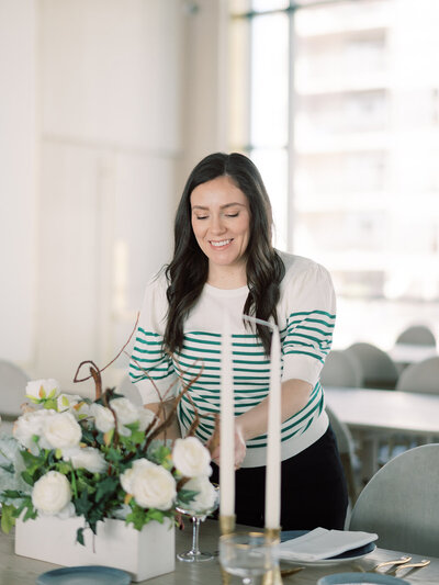 Carina, from Corporate Events Hamilton wearing a white and green striped shirt placing a table setting  at the Pearle Hotel