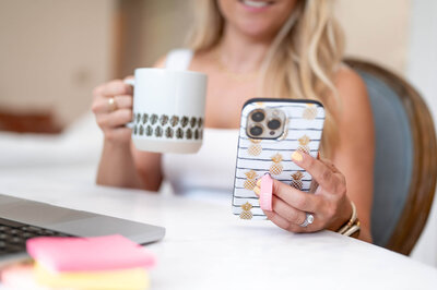 Close up shot of a woman's hands holding a cell phone in one hand, and a coffee cup in the other.