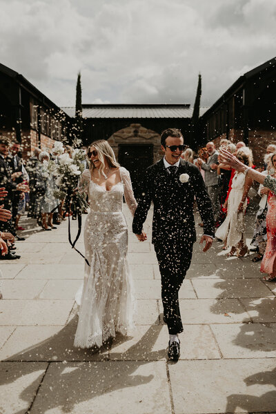 A cool bride and groom walk down the line as their guests throw confetti. . 