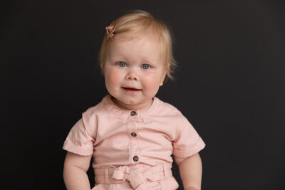 baby girl looks into camera in simple portrait against black wall at studiostudio in ann arbor michgian