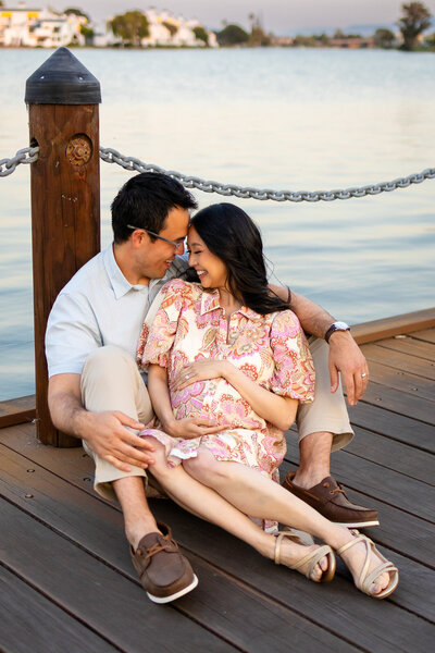 Expecting couple cuddles on a dock at sunset during maternity session by Ellobelle Photography, capturing joy and connection by the water.