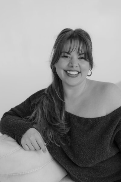 woman smiling with her arm rested on the back of the chair 