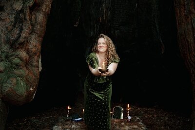 Oracle Business Witch Rachael Maddox stands in front of a huge tree with a cavernous hole in the trunk. Teaching business magick and money magick, guiding entrepreneurs to release hustle energy and fund their world-changing visions.