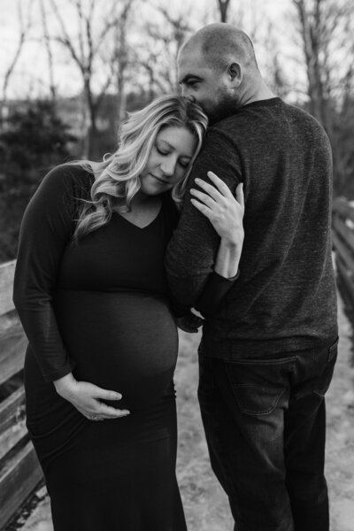 pregnant woman holding her stomach and leaning against her partner who is kissing her head