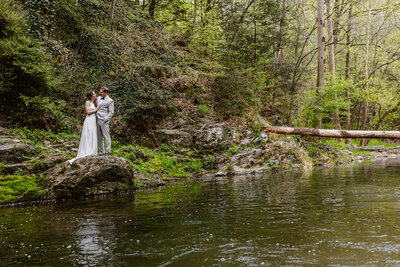 A bride and groom stand on a rock in a stream on their elopement day at Drumore Mill 