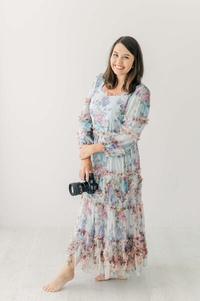Katiera standing in a blue and pink dress holding her camera smiling