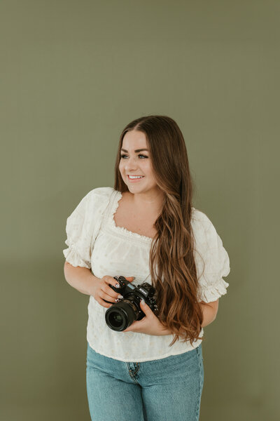Branding photo for Bailee Freeman Photography with a black blazer and a Nikon camera in front of her. 