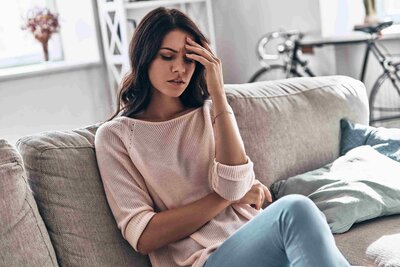 Femme fatiguée et souffrante assise sur un canapé – accompagnement thérapeutique à Montréal en physiothérapie, ostéopathie et coaching pour comprendre la douleur et retrouver la santé globale
