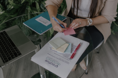 A close-up view of hands writing on a desk with a notebook and pen, illustrating the dedicated and detail-oriented approach of Creative Dynamics' virtual assistant services in Canada and the USA. This image represents the meticulous attention to detail we provide in managing your tasks and supporting your business needs.Photo courtesy of Unsplash.