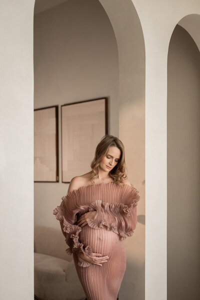 Zwangerschapsshoot van een vrouw in een elegante roze jurk, draaiend in de iconische bogen van Studio Laurant in Arnhem, vastgelegd door Juliette Fotografie.