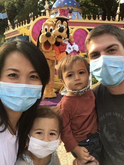 Family with two kids with masks posing with goofy and pluto at Disney