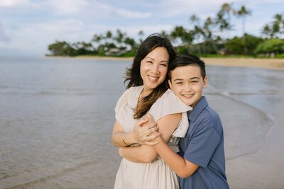 A mother and son hug on the beach.