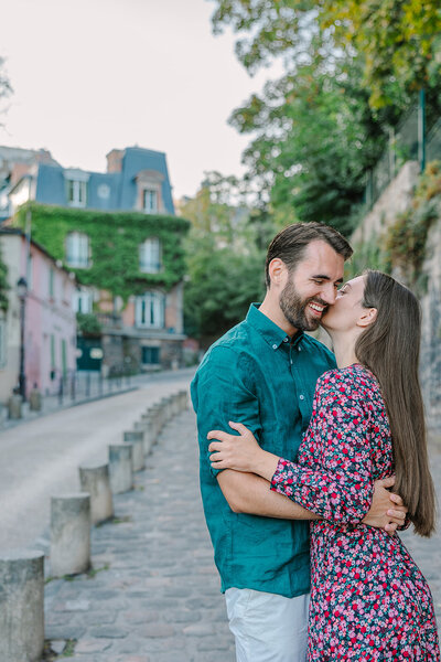 Woman kissing her partner’s cheek as they hug during a romantic Paris couples photoshoot on rue de l’Abreuvoir in Montmartre.