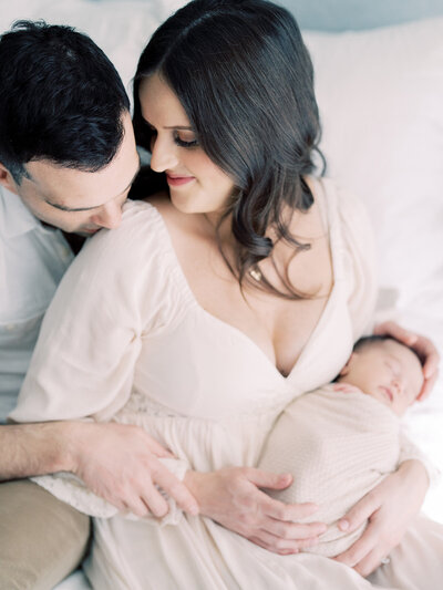 A brown-haired mother holding her newborn leans into her husband as he kisses her shoulder photographed by Maryland Newborn Photographer Marie Elizabeth Photography