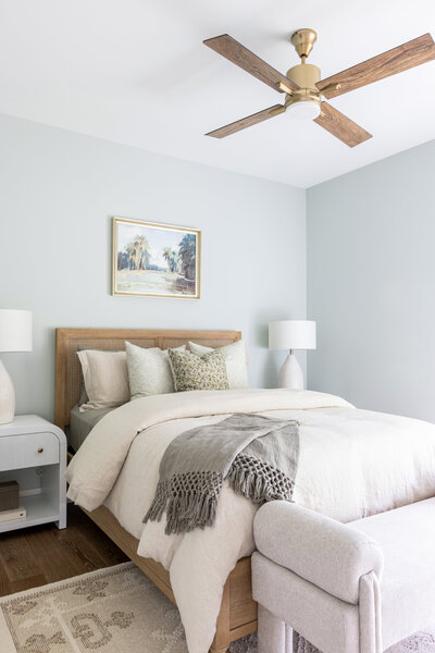 Coastal guest bedroom with  cane bed, neutral bedding and sage green accents.