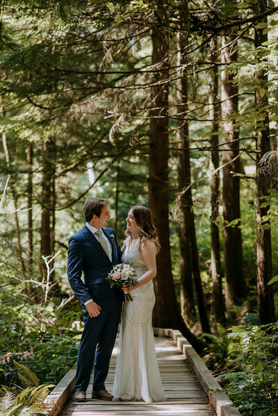 A bride and groom wearing a yellow and green puffy jacket hold each other on top of Rainbow Glacier in Whistler. There is snow all around and blue skies.