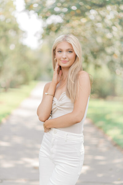 Beautiful blonde senior stands in a beautifully lit tree lined sidewalk, perfectly posed for senior portraits in Baton Rouge, LA.