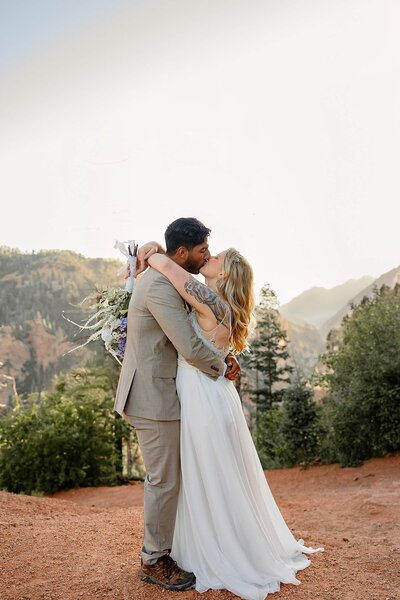 Bride and groom with arms around each other kissing. Gorgeous mountain scenery