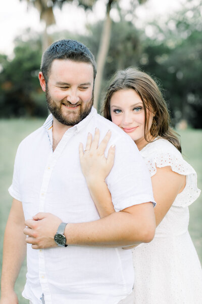 Woman hugging man from behind in a park in an engagement photography session taken by Tampa photographer, Tina Marie