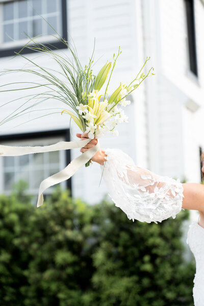Photographer takes a picture of the bride holding bouquet of white and green flowers in front of white church in North Carolina. Part of wedding photography 