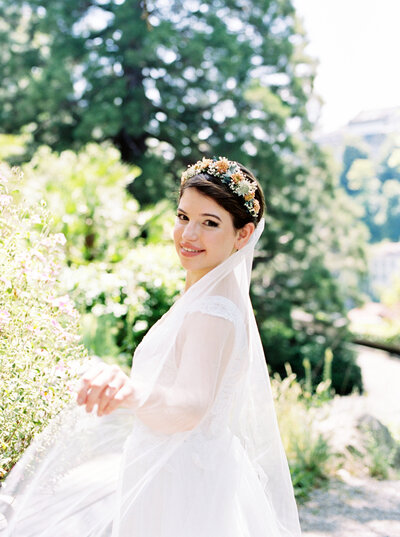 Bride looks over her shoulder wearing floral headband and veil