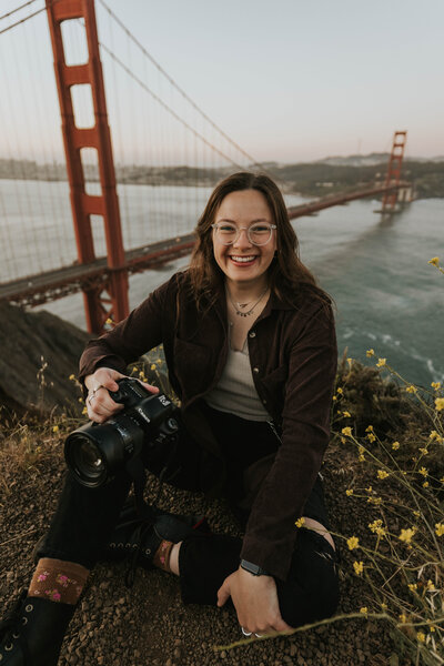 woman smiling while holding camera with golden gate bridge in background