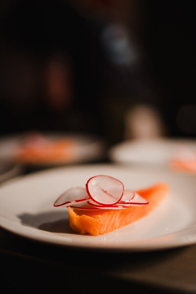 Close-up of a salmon fillet topped with thinly sliced radish on a white plate at Sael Birmingham.