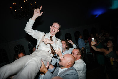 Wedding guests holding up a groom at the reception