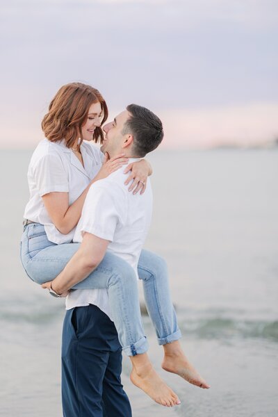 Groom picking up and kissing bride in ocean waves