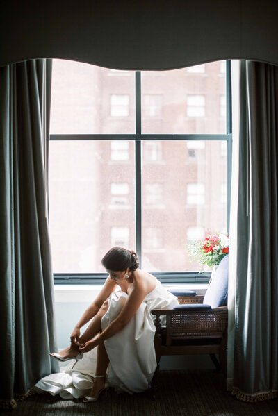 Groom embracing the bride from behind in a lush garden, bride’s bouquet of red, pink, and white flowers resting on the groom’s shoulder.