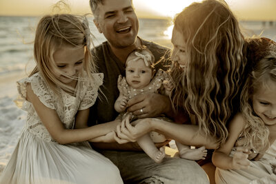 Family Photographer, A small family huddle together at the beach, a mother, father, daughter, and baby sister