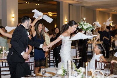 A newlywed couple holding hands and dancing through their wedding reception 