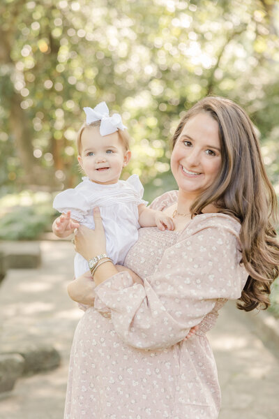 Pregnant mother in pink dress holding her toddler girl smiling for portrait by Maternity Photographer Greenville SC