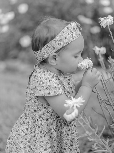 Girl with a dress smelling a white flower outside.