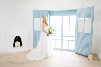 Beautiful bride poses next to light blue door holding wedding bouquet