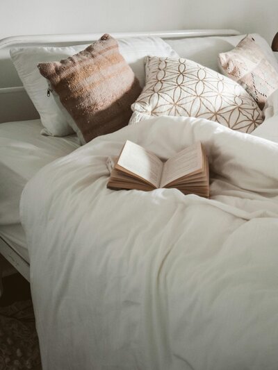 A cozy bed with a soft white blanket and a book resting on top.