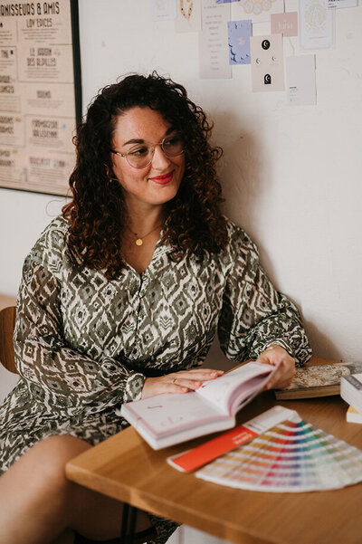 Alexiane Maupetit est souriante en train de feuilleter des livres de graphisme.
